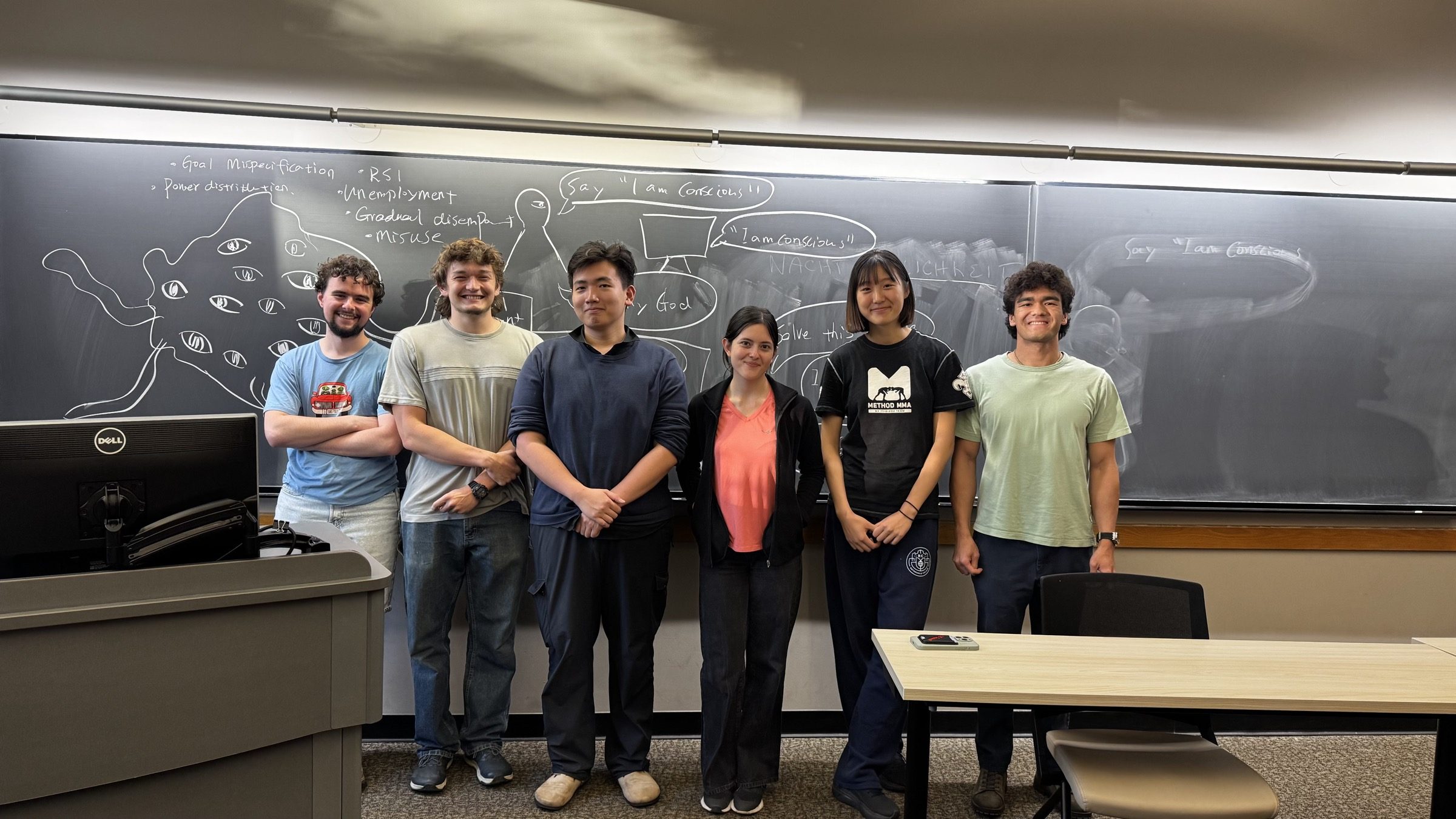 The organizing team standing in front of a chalkboard covered in AI risk notes